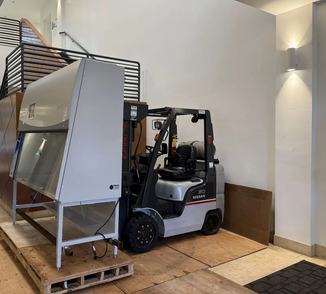 Biosafety cabinet on a reinforced custom pallet beside a forklift in a Bay Area biotech building lobby, with plywood floor protection laid for the laboratory relocation